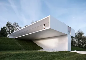 A minimalist white concrete house on a grassy hill.