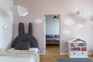 Children's bedroom featuring pink walls with white paper clouds, a bed with a bunny-shaped headboard, and a small white dollh