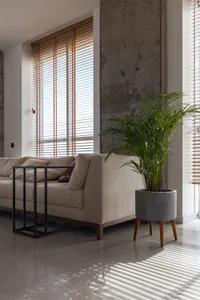 Contemporary living room with concrete walls, wooden floor, and fabric furniture, featuring vertical blinds.