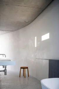 A modern bathroom with a concrete wall, minimalistic design, and a stool.