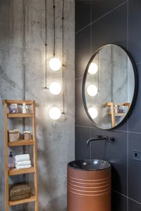 Modern bathroom featuring a round mirror with spherical lights, a wooden shelf with toiletries, and a black sink.