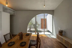 Modern dining room featuring wooden furniture, a arch window leading to an outdoor space, and warm lighting.