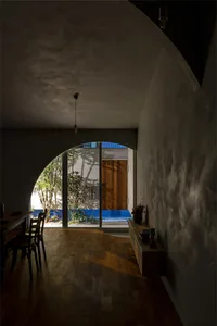 A spacious, modern interior with concrete walls and wooden flooring, featuring a dining area and a view through an archway to