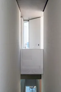 A modern minimalist interior with concrete walls and white furnishings, featuring a sink area with a window and a chair in th