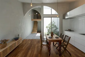 A modern residential dining space featuring wooden furniture, tile flooring, and an arched doorway leading to a staircase.