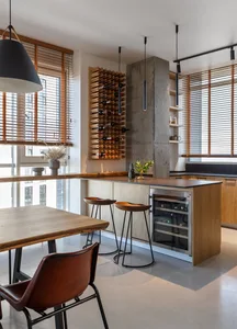 A modern kitchen featuring a wooden wine rack and bar stools, with natural light streaming in through the large windows.