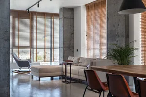 A modern living room featuring concrete walls, glass elements, and wood blinds.