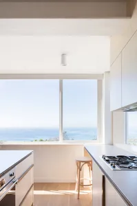 A minimalist kitchen with white cabinets and a large window overlooking the ocean.