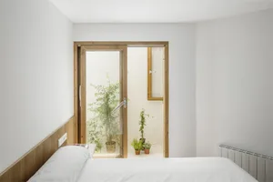 Modern minimalist bedroom with white walls, wooden headboard, and potted plants.