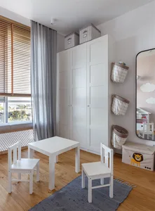A minimalist children's room featuring a wooden table and chairs, white furniture, and fabric storage baskets.