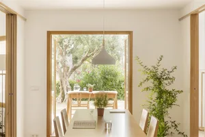 Minimalist dining room with wooden table and chairs, large window with lush greenery outside