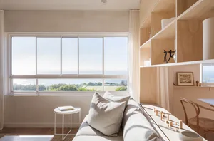 A minimalist living room with a wooden shelving unit and a sofa facing a large window with a sea view.