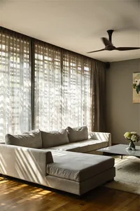 Modern living room featuring neutral-colored furniture, sheer white curtains, and a white marble coffee table with a vase of 