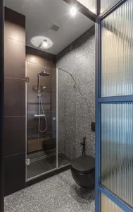 A modern minimalist bathroom featuring metallic textured black tiles, a sleek shower enclosure, and a toilet with black accen
