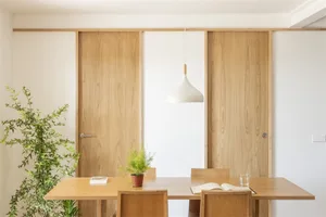 Interior of a modern minimalist dining room featuring a wooden table, chairs, and pendant lamp.
