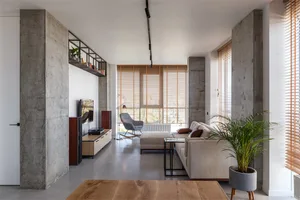 Modern, minimalist living room with concrete walls and floor, white couch, and floor-to-ceiling windows.