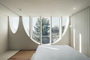 A modern bedroom featuring a large oval window with a view of trees and a city skyline.