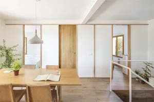 Modern residential dining room with wood and white interior, featuring a hanging light fixture and open layout.