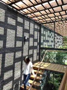 A modern staircase with glass railings and wooden treads, featuring a black brick wall with geometric patterns created by sun