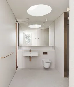 A modern, minimalist bathroom with white tiled walls and floor, a sink, and a toilet.
