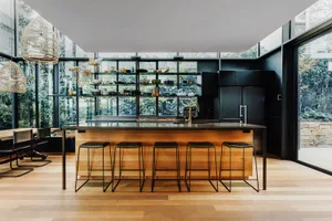 A modern kitchen with black shelves, a wooden counter, and a large window overlooking greenery.