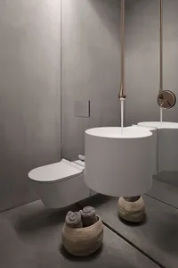 A sleek, modern minimalist bathroom featuring a white ceramic toilet and sink, with a metallic tap and a basket of gray towel