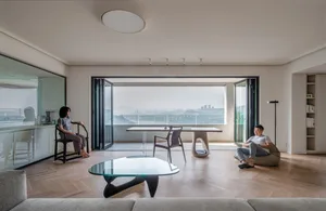 Two individuals in a minimalist living room with glass doors overlooking a cityscape.