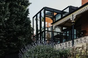 A modern house with large glass windows and a brick facade surrounded by lush greenery and purple flowers.