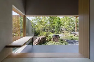 A view of a serene outdoor garden with rocks and plants seen through a large window of a minimalist interior design.