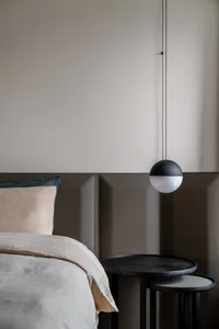 Modern minimalist bedroom with a neatly made bed featuring light-colored bedding, a hanging light fixture, and fabric-paneled