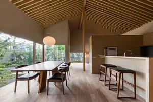 Modern minimalist kitchen with wood flooring and countertops, featuring black chairs and a long table.