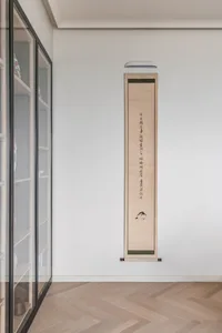 A minimalist interior featuring a paper scroll with Chinese calligraphy hanging on a white wall.