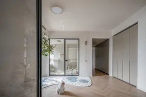 A minimalist interior with white wood flooring and a white cat sitting in the foreground.