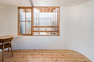 A minimalist living room featuring wooden flooring and a large window with a wooden frame.