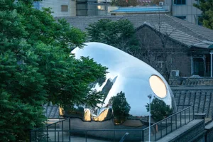 A minimalist metal sculpture with a smooth, polished surface and a circular window.
