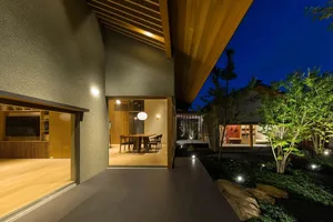 A minimalist residential interior with a wooden dining table and chairs, surrounded by a beautifully landscaped outdoor area.
