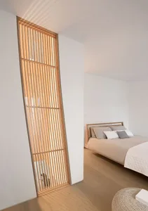 A modern bedroom featuring a wooden bed frame and floating headboard with a grid of vertical wooden bars, illuminated by natu