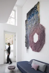A modern entryway featuring a large, textured yarn wall art with a circular cut-out and blue, pink, and beige colors.