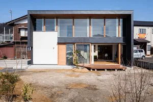A modern house with large glass windows and wooden accents set against a clear blue sky.
