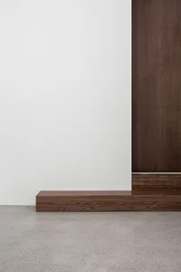 A modern interior featuring a wooden floor, contrasting with a white wall and a wooden vertical panel.