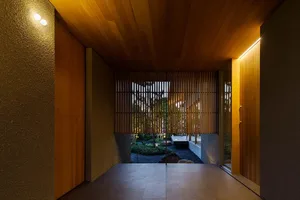 A modern interior space with wooden walls and a stone floor, featuring a view into a serene courtyard.