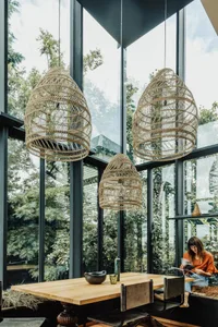 A modern living room with cane pendant lights and a large glass window overlooking greenery.
