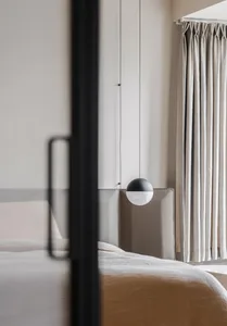 A modern minimalist bedroom featuring a white bed with cotton bedding, a dark gray headboard, and a circular pendant light.
