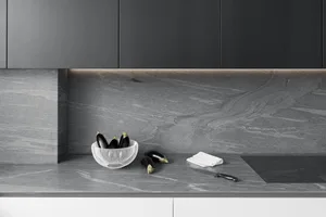 A modern minimalist kitchen with a black stone countertop featuring a bowl of eggplants, a knife, and a white napkin.