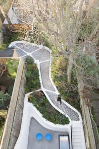 A modern garden pathway with stone-paving, surrounded by greenery and trees.