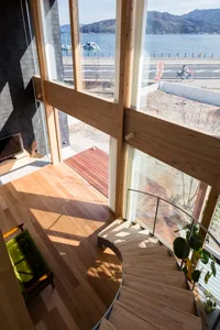 Minimalist style staircase with wooden stairs and railings seen from above, featuring a view of a body of water and a road in
