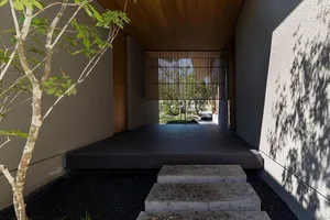 Concrete entrance with wood slat screen and plants, leading to a garden.