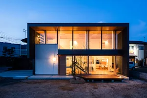 Modern house exterior with wood, concrete, and large glass windows at dusk.