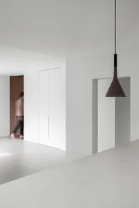 Modern minimalist apartment with concrete walls and floor, featuring a person walking past a door.