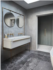 Modern bathroom with concrete walls and floor, featuring a white vanity with brass fixtures and double mirrors.
